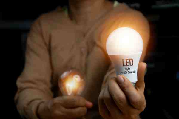 Person compares glowing incandescent bulb with an energy-saving LED bulb.