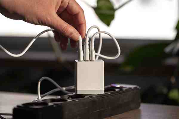 A person plugs a white USB cable into a multi-port charger on a power extension board, showing energy-efficient charging.