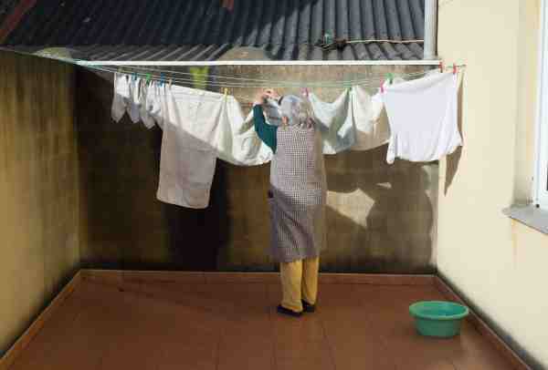 Elderly woman air-dries clothes in sunlight, showing weather supports energy-efficient habits.